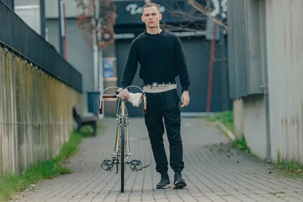 Bisikletli genç adam sokakta yürüyor.