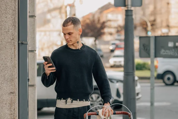Sokakta bisikletli, cep telefonu olan şehirli genç bir adam.