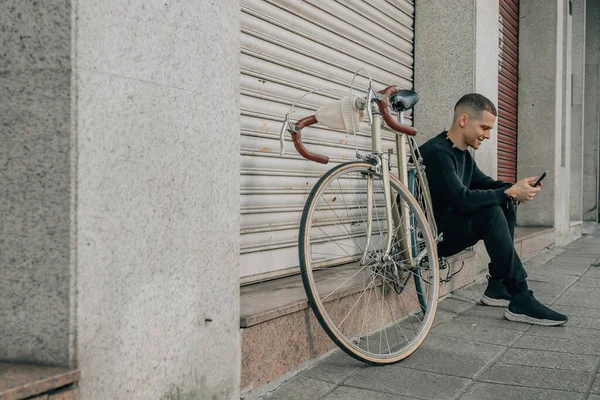 Genç adam cep telefonuyla sokakta oturuyor.