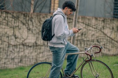 Mobil ve sırt çantalı genç adam ya da öğrenci klasik bisiklete biniyor.
