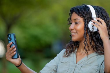 Güzel, genç bir Latin kadın cep telefonu ve kulaklıkla gülümsüyor.