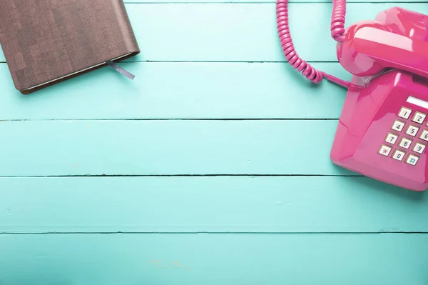 Classic pink telephone receiver with notebook, waiting phone call, Retro telephone and book on old green wooden floor.