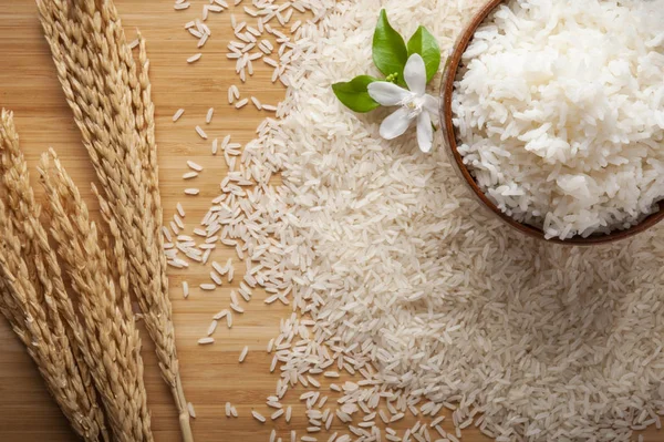 Top view of jasmine rice in a bowl on dark wooden table with rice plants, jasmine flower, ear of rices with jasmine rice in a bowl , rice scatter on the floor.