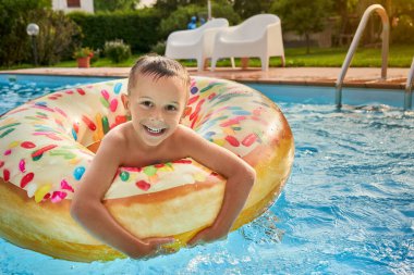 Şişirilebilir renkli yüzükte yüzme havuzunda 5 yaşında bir çocuk.