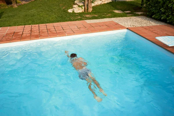 Garçon nageant dans la piscine ouverte en été Image En Vente