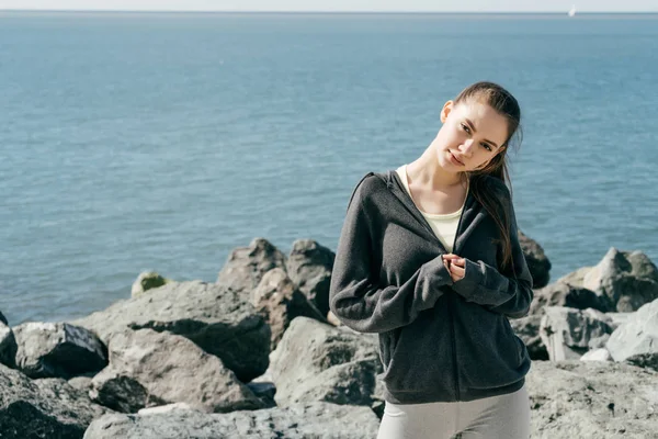 Mooie sportieve meisje in stijlvolle zwarte kleding poseren in de zon bij de zee — Stockfoto