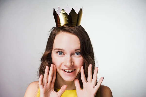 Mooi blauwogige meisje in een gele jurk glimlacht en kijkt naar de camera, op haar hoofd een gouden kroon — Stockfoto