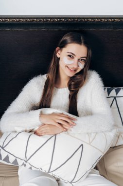 gülümseyen mutlu uzun saçlı kız yatakta sabahın erken saatlerinde, beyaz lekeler, gözleri altında oturan beyaz pijama