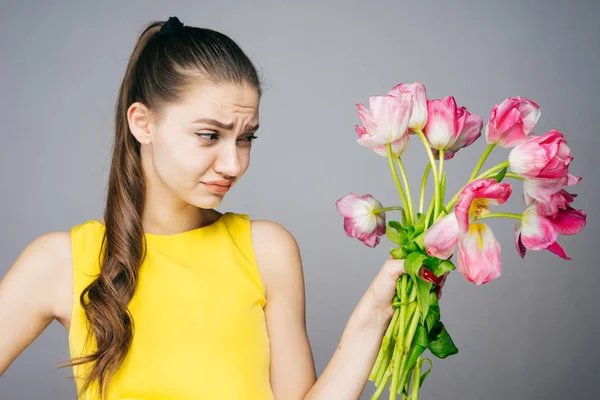 Mujer joven insatisfecha en vestido amarillo sostiene un ramo de flores rosadas en las manos — Foto de Stock