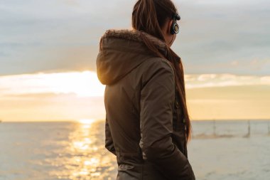 genç bir kız güç ve enerji, gün batımında, deniz kenarında yürüyüş önce kulaklıklar müzik dinlemek alır