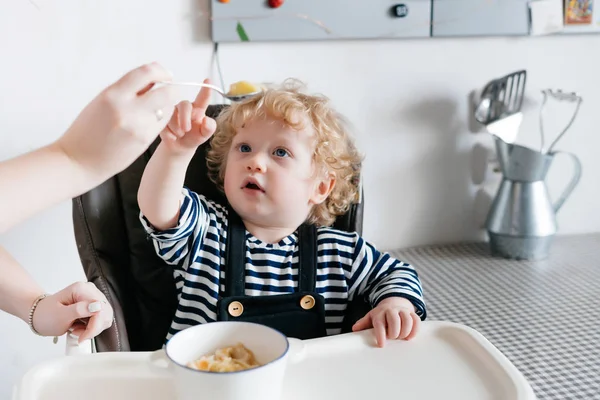 가족 아침 식사, 작은 곱슬 머리 아이 부엌에서 어린이의 자에 앉아서 그의 어머니와 함께 건강 한 죽 먹고 — 스톡 사진