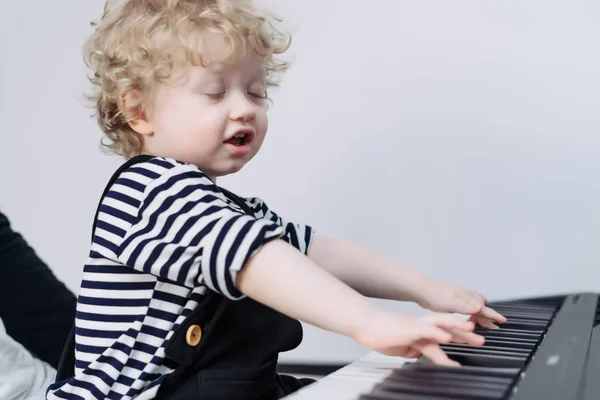 Cute little curly baby boy learns to play the piano, exploring the world — Stock Photo, Image