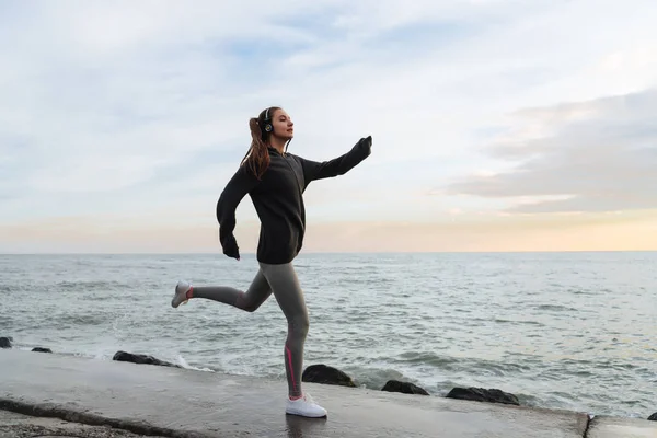 Självsäker snabbt ung flicka springer runt strandpromenaden och lyssnar på musik i hörlurar — Stockfoto