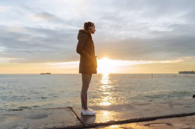 Sakin, ince kız koşu önce güç alır, akşam güneş ışınlarının deniz standları ve kulaklıklar müzik dinler