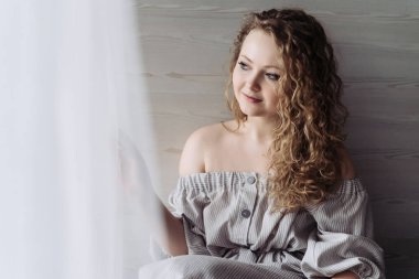 bir yaz aylarında sevimli kıvırcık saçlı bir kadın elbise gülümsüyor ve görünüyor pencereden, bir şey hakkında düşünüyor iyi