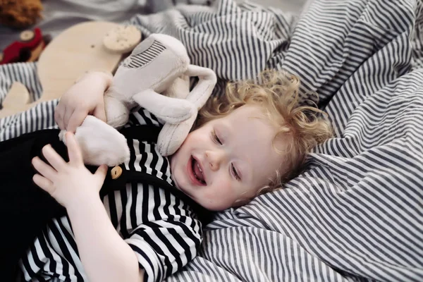 Směje se kudrnaté miminko chlapeček ležel v posteli s jeho hračkami baví — Stock fotografie
