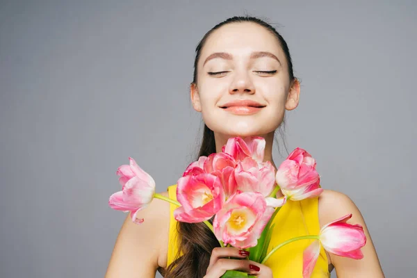 Linda chica joven feliz en vestido amarillo celebra el día de la madre, huele fragantes flores de color rosa — Foto de Stock