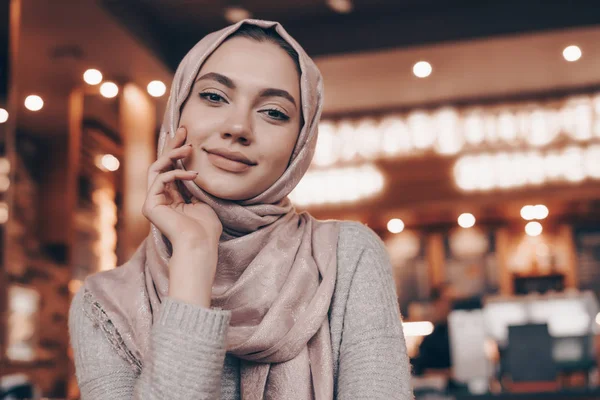 Aranyos fiatal muszlim lány ül egy arab kávézó, látszó-on fényképezőgép, és mosolyogva fejkendő — Stock Fotó