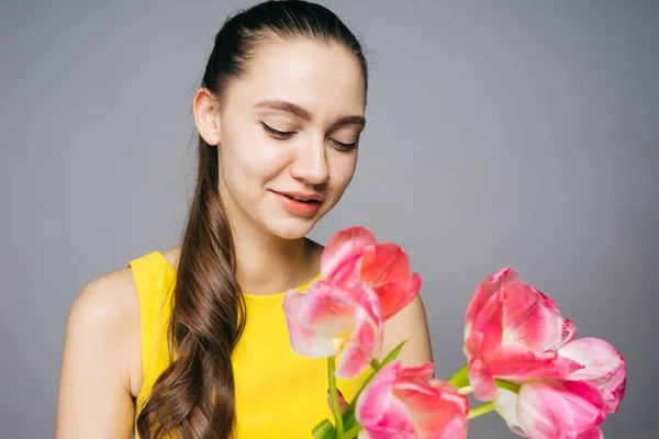 Beautiful young girl in yellow dress is holding in hands a fragrant pink flowers and smiling — Stock Photo, Image