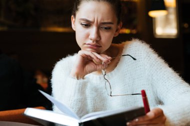 dalgın hüzünlü genç kız freelancer beyaz ceket içine onun defter arayan bir kafede oturuyor