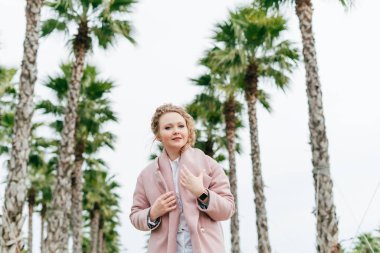 Park ve gülümsüyor, yeşil bahar moda pembe ceket kıvırcık kadın yürür bir genç aittir