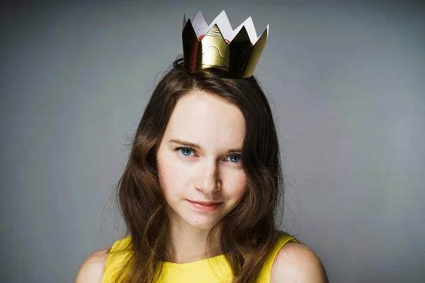 Bela jovem elegante em um vestido amarelo olha para a câmera, na cabeça uma coroa de ouro — Fotografia de Stock