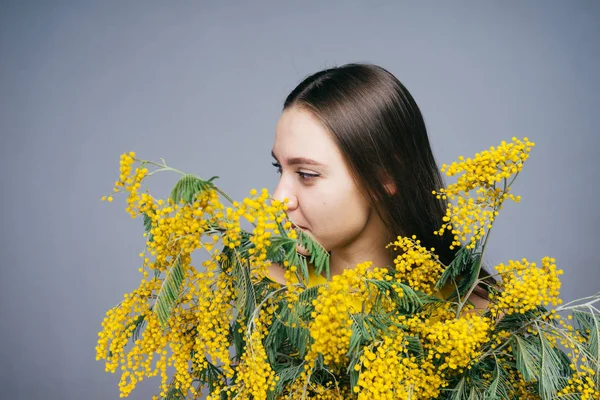 Carina giovane ragazza che tiene un mimosa giallo fragrante nelle sue mani, godendo la primavera — Foto Stock