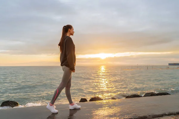 Den atletiska unga flickan gick en joggingtur intill havet på kvällen på solnedgången, tåg och leder en hälsosam livsstil — Stockfoto