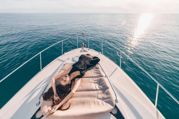 Lussuosa ragazza in abiti estivi neri sdraiata sul suo yacht bianco e riposante, godendo la vita ricca e il calore — Foto Stock