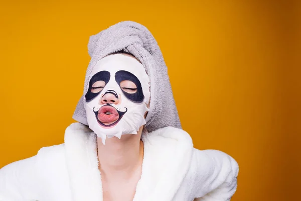 Grappig meisje met een handdoek op haar hoofd en in een badjas wil zijn prachtige, gezichts masker met Panda gezicht — Stockfoto