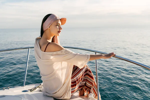 Egy gazdag fiatal nő egy kendő, a fején ül egy fehér jacht, élvezi a tengeri utazás és a meleget — Stock Fotó
