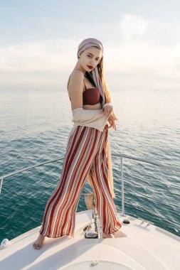 onun beyaz yatta, uzun zamandır beklenen tatil poz trendy yaz pantolonlu güzel zarif kız