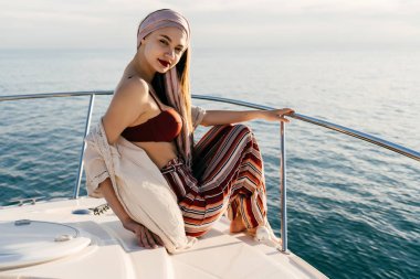 güzel çekici kız bir başörtüsü ile beyaz bir yatta oturur, bir adada tatil yelken