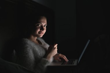 Laptop korku filmi izlerken karanlıkta, gece geç saatte yatakta oturmuş sevimli genç kız