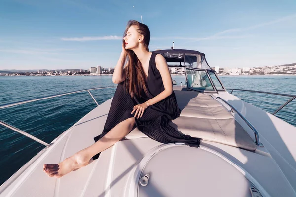 Una atractiva mujer de pelo largo con ropa negra descansa en su yate blanco, nada a lo largo del mar azul tranquilo —  Fotos de Stock