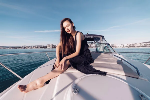 beautiful rich woman in black clothes sits on her white yacht, enjoys rest and leave