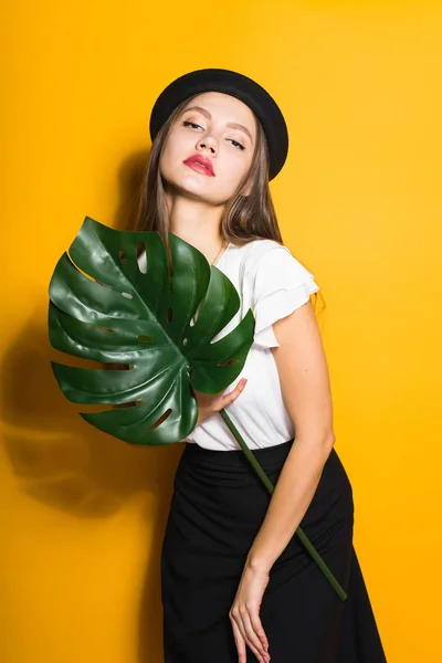 Atractiva joven modelo en sombrero negro sostiene una hoja verde y poses, estilo y moda — Foto de Stock