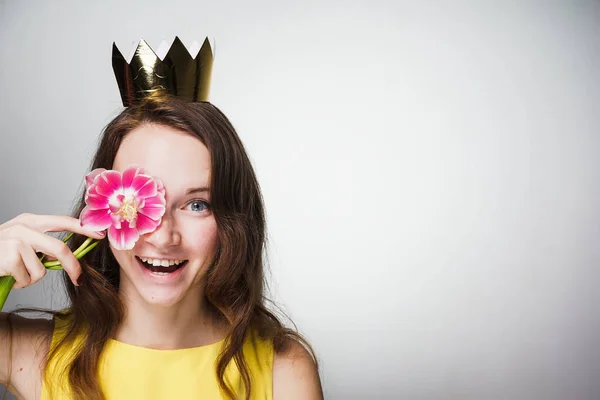 Divertida mujer joven en vestido amarillo sostiene fragante flor rosa cerca de la cara y sonrisas — Foto de Stock