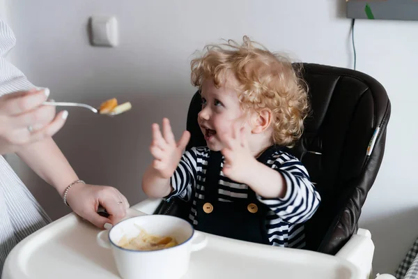 Заботливая мать кормит своего маленького сына вкусным супом, на кухне, семейный ужин — стоковое фото