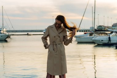 şık uzun saçlı kız moda bej bir palto bir liman ve onun yat bekliyor