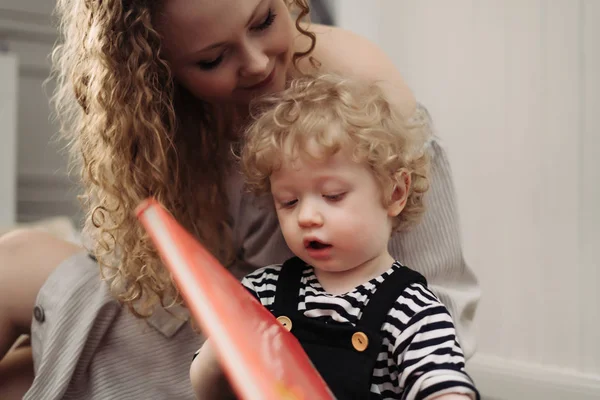 Curly, careful young mother spends time with her little son, teaches reading — Stock Photo, Image