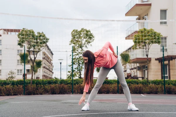 Активная молодая девушка разминает мышцы перед тренировкой на спортивной площадке, хочет похудеть — стоковое фото
