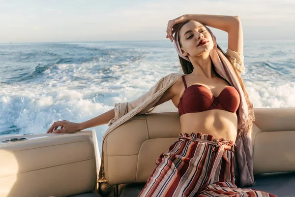 Una joven de lujo en ropa elegante disfruta de un viaje por el mar en un yate, posando en los rayos del sol —  Fotos de Stock