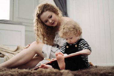 bakım genç bir anne küçük kıvırcık oğlu ile yere oturur, onu okumayı öğretir