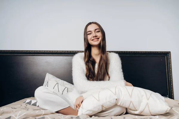 Glückliches junges Mädchen im Pyjama sitzt frühmorgens im Bett, gut gelaunt, lächelnd — Stockfoto