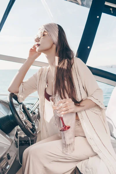 A luxurious elegant woman in stylish summer clothes sails on her chtte along the Caribbean sea, enjoys a rich life and drinks champagne — Stock Photo, Image