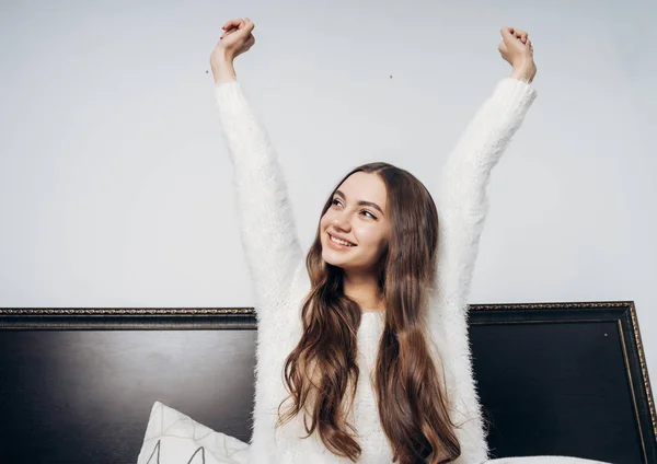 Feliz chica de pelo largo en pijama blanco se despertó temprano en la mañana, se estira y se inquieta por un nuevo día — Foto de Stock