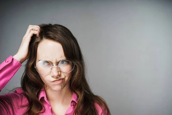 Trabajadora de oficina joven pensativa seria en camisa rosa y gafas se rasca la cabeza y piensa en el trabajo — Foto de Stock