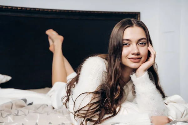 Schönes junges Mädchen mit langen Haaren im Schlafanzug liegt frühmorgens im Bett, gute Laune — Stockfoto