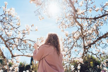 kıvırcık zarif kadın şık pembe ceket bahar parkta yürüyor ve çiçekler ve sıcaklık sahiptir